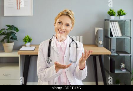 Smiling female doctor with stethoscope, offering consultation in modern office Stock Photo