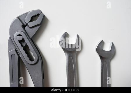 Top view of an adjustable wrench, water pump pliers with red handles, and two combination spanners arranged on a white surface. Stock Photo
