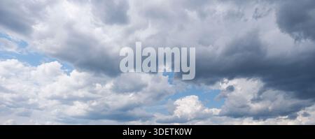 Wide panoramic shot of intense sky filled with dark, dramatic cumulus clouds and contrasting bright white clouds, with patches of bright blue sky show Stock Photo