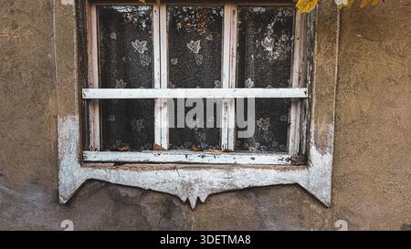Front view of an aged wooden window frame with peeling paint on a traditional clay-walled house in Moldova. Stock Photo