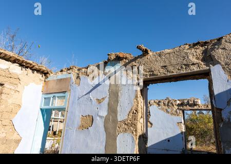 Weathered mud brick walls with peeling plaster and open doorways under a clear blue sky, evoking themes of abandonment and decay. Stock Photo