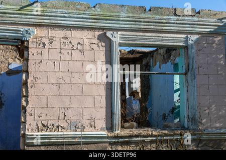 Close-up of a dilapidated wall with peeling paint and broken window frames, revealing an empty interior, ideal for themes of decay, history, or urban Stock Photo