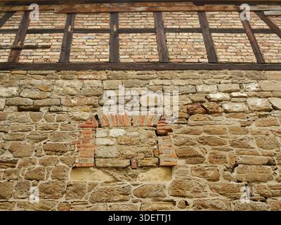 Stone façade of old building with bricked-up arched opening and half-timbered upper floor. Historic detail. Copyspace. Stock Photo