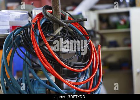 Messy electrical wires hanging on metal rod in industrial workshop with colorful tangled bundle of red blue black cables showing disorganized chaos an Stock Photo