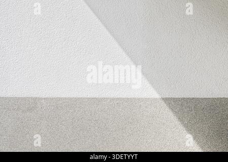 Diagonal sunlight casts a shadow across a textured two-tone wall in Munich, Germany. The minimal composition emphasizes geometry, light, and surface detail. Stock Photo