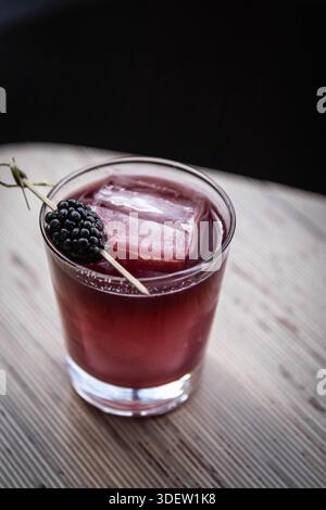 Blackberry cocktail with large ice cube on wooden table Stock Photo