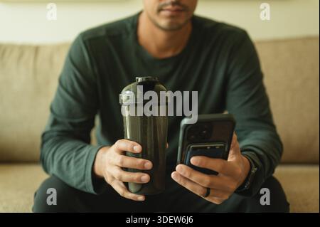 Young man holding protein shaker and tracking fitness on phone Stock Photo