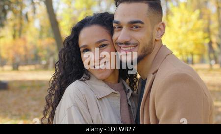 Close-up hispanic couple in love looking at camera in autumn park city portrait touching faces cheeks smiling enjoying love Arabian guy and girl happy Stock Photo