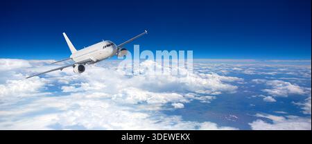White airplane flying high in a deep blue sky above a blanket of clouds Stock Photo