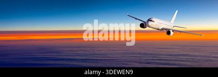 White passenger airplane cruising above the clouds with a vibrant orange and blue sky Stock Photo