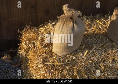 A tied hessian burlap sack resting on a bale of dry straw in sunlight Stock Photo