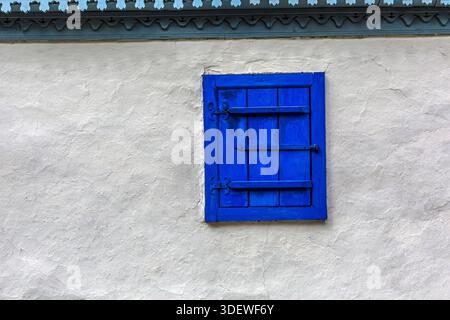 Blue window shutters closed on a white stucco wall with decorative wood trim Stock Photo
