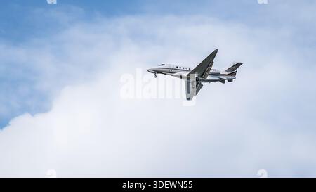 A Cessna Citation Latitude business jet flies against a dramatic cloudy sky, captured in black and white. Stock Photo