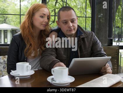 Two students drinking coffee and having fun with tablet In cafeteria Stock Photo