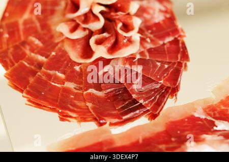 Close-up of thinly sliced cured ham arranged in overlapping layers, showing texture and rich color. Stock Photo