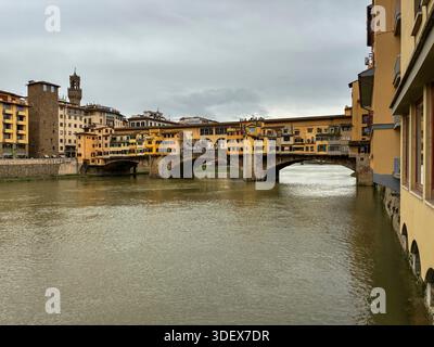 Italy, Florence, Tuscany. The Ponte Vecchio spans River Arno. Buildings line historic bridge. Water murky. Stock Photo