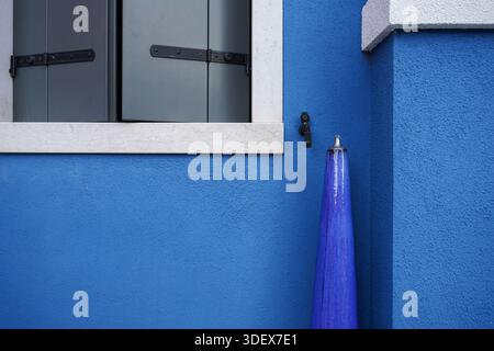 Burano, Italy, minimalism, vibrant blue painted wall, closed window shutters, tapered decorative object, abstract geometry Stock Photo