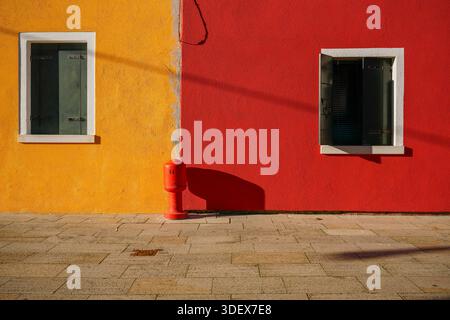 Burano, Italy, minimalism, yellow and red walls, two windows, fire hydrant, strong sunlight, geometric contrast Stock Photo