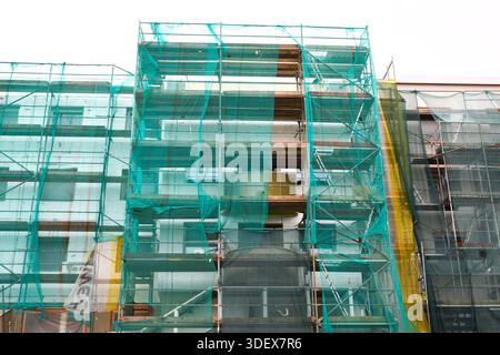 Building Under Renovation with Full Scaffolding and Green Safety Netting, Showing Structural Work and Protective Measures in an Urban Construction Zon Stock Photo