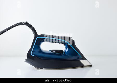 Steam iron with side view resting on white table with reflection and white isolated background. Front view. Stock Photo