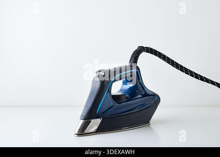 Front side view of blue steam iron reflected on white table and white isolated background. Front view. Stock Photo