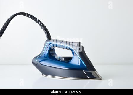 Detail of side view of blue steam iron resting on white table and white isolated background. Front view. Stock Photo