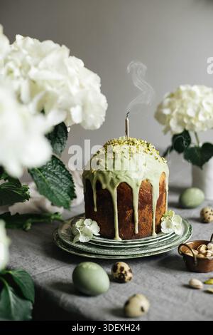 Homemade traditional Russian Easter bread Kulich with pistachio glaze decoration. Vintage tablecloth. Hydrangea flowers. Stock Photo