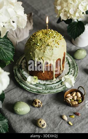 Homemade traditional Russian Easter bread Kulich with pistachio glaze decoration. Vintage tablecloth. Hydrangea flowers. Stock Photo