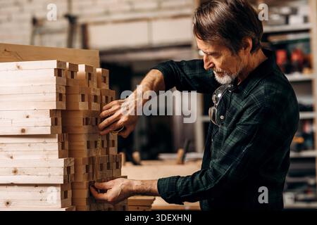 Senior carpenter using measuring tape on a bunch of wooden parts || Model released Stock Photo