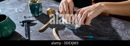 Young woman focuses on molding clay in a pottery studio, immersed in her artistic hobby. Stock Photo