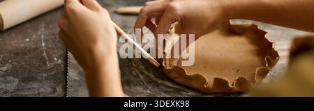 A young woman focuses on sculpting clay at her pottery studio, immersed in creativity and passion. Stock Photo
