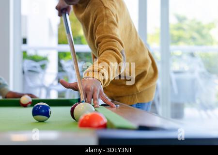 Two men including mustard-sweater man leaning over green-felt pool table lining up cue at home Stock Photo
