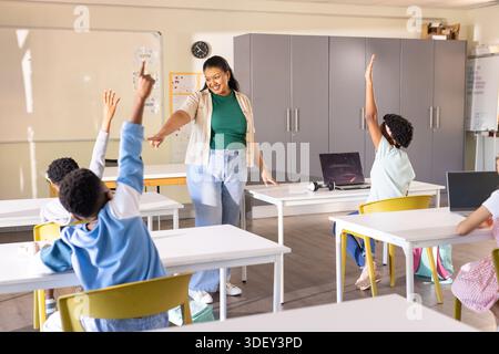 African American teacher in jeans pointing to raised hands engaging youth with laptops in class Stock Photo