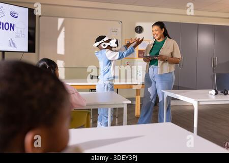 Teacher with students guiding boy wearing VR headset while holding tablet in classroom Stock Photo