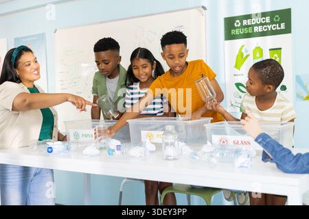 Diverse group with Hispanic teacher pointing, children sorting into clear labeled bins in classroom Stock Photo