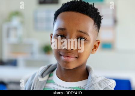 African youth male sitting in classroom wearing gray hoodie and striped shirt near bulletin board Stock Photo