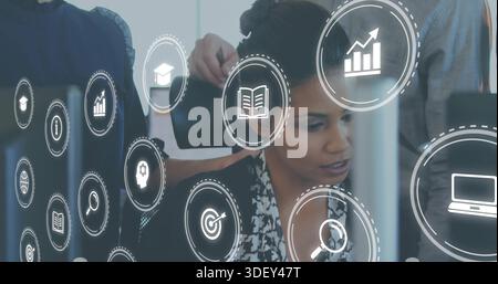 Reviewing mid-adult woman focusing on computer at office, wearing dark blazer, showing glass icons Stock Photo