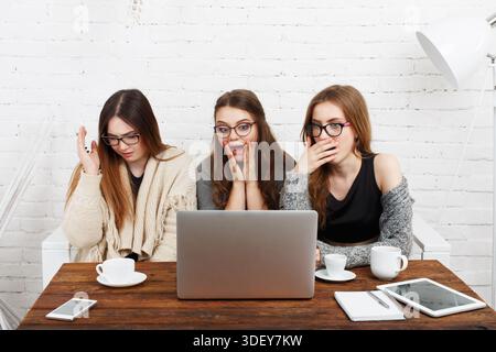 Three Women React to Surprising Content on a Laptop During a Casual Gathering in a Bright Room Stock Photo