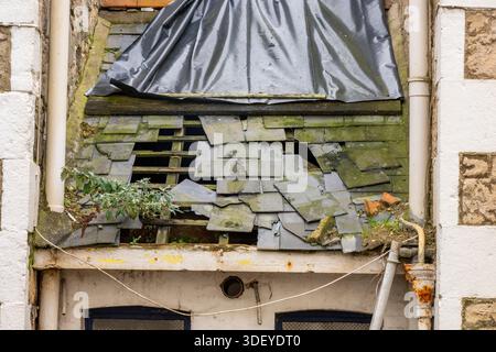 Badly damaged roof with missing tiles and slates following a storm with high winds, storm damaged roof on old building with missing slates and tiles. Stock Photo