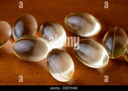 Macro shot of yellow liquid vitamin capsules on a brown wood background. Concept of dietary supplements, daily healthcare, and wellness routine. Stock Photo