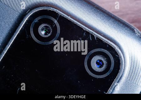 Extreme detail of a broken mobile phone camera glass with visible cracks and scratches. Rusty and damaged electronics concept for tech repair. Stock Photo