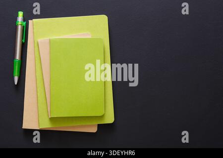 Collection of Green Notebooks and a Pen Arranged on a Black Surface Stock Photo