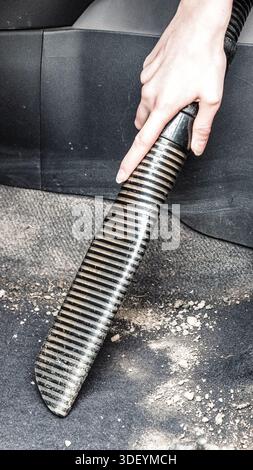 Hand using vacuum cleaner to clean car interior upholstery, removing dust and dirt as part of vehicle maintenance and detailing. Stock Photo
