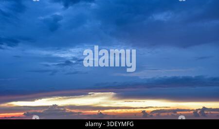 Clear and vast blue sky featuring a thin but intense band of golden sunlight and small clouds at the bottom of the horizon. Stock Photo