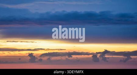Dramatic evening sky showing distinct horizontal layers of dark clouds and a brilliant, glowing golden band of light at the horizon. Stock Photo