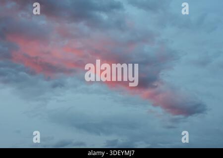 A peaceful and minimalist evening sky featuring a soft blue gradient and a delicate, illuminated pink cloud during late afternoon. Stock Photo
