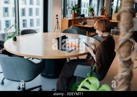 Middle age female using smartphone during quiet work moment indoors Stock Photo
