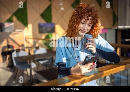 Mid adult female nurse taking a break in the hospital cafeteria, using a phone while enjoying a moment of relaxation Stock Photo