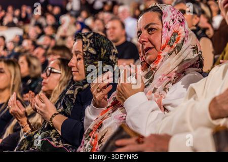 At the end of the Şeb-i Arus ceremony at the Mevlana Kültür Merkezi in Karatay, Konya, Turkey, a venue that holds up to 3,000 people, the spectators are also moved: two women in colourful headscarves applaud, visibly touched, among the audience. Şeb-i Arus is the annual festival marking the death anniversary (17 December) of the mystic poet Rumi (Jalāl ad-Dīn ar-Rūmī, 1207–1273), founder of the Mevlevi order, celebrated as a spiritual union with God. Stock Photo