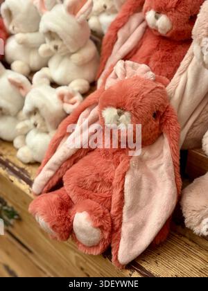 Close-up of cute plush bunny toys in pastel pink and terracotta colors on a wooden shelf. Stock Photo